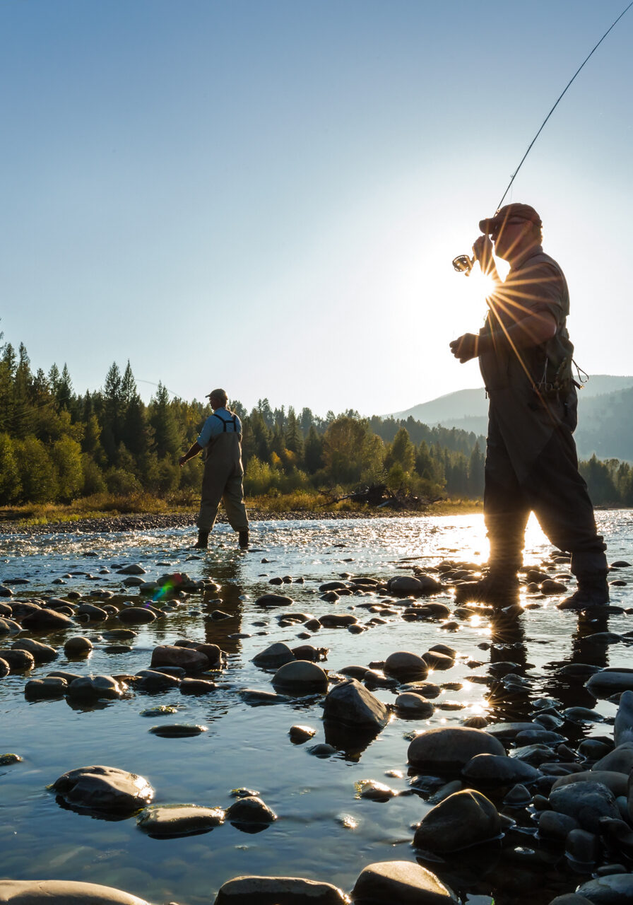 Two people fishing in a river with rocks.